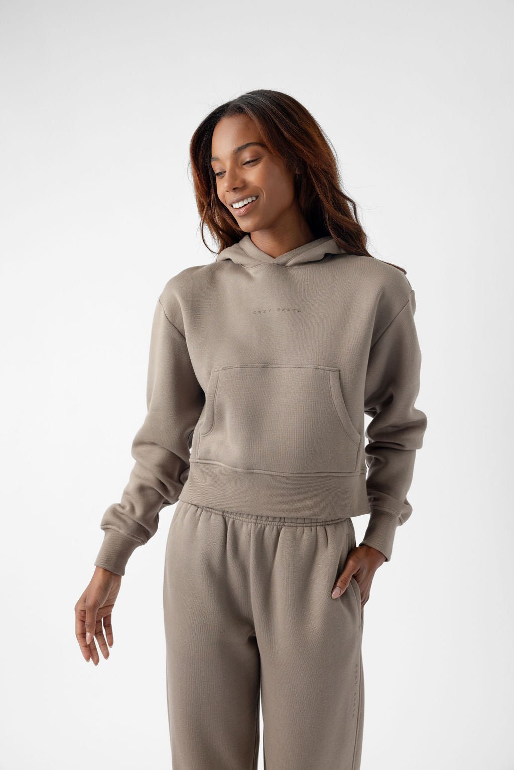 Person wearing a beige hoodie and matching sweatpants, smiling with a relaxed pose.