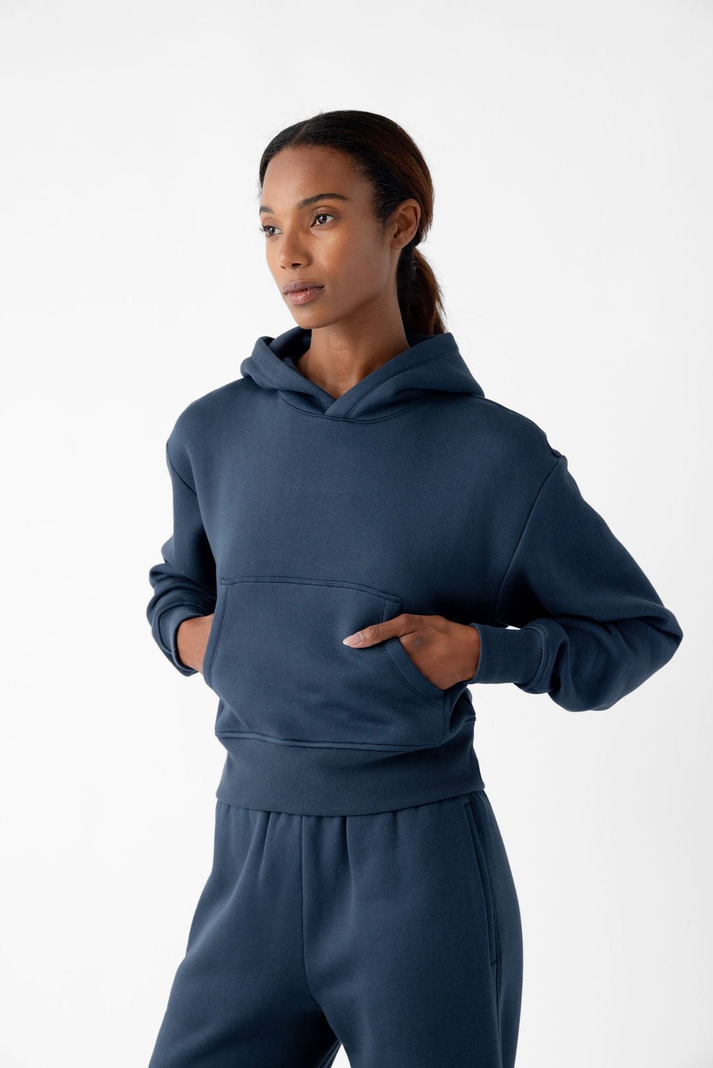 Woman wearing a navy blue hoodie and matching sweatpants, with hands in front pocket.