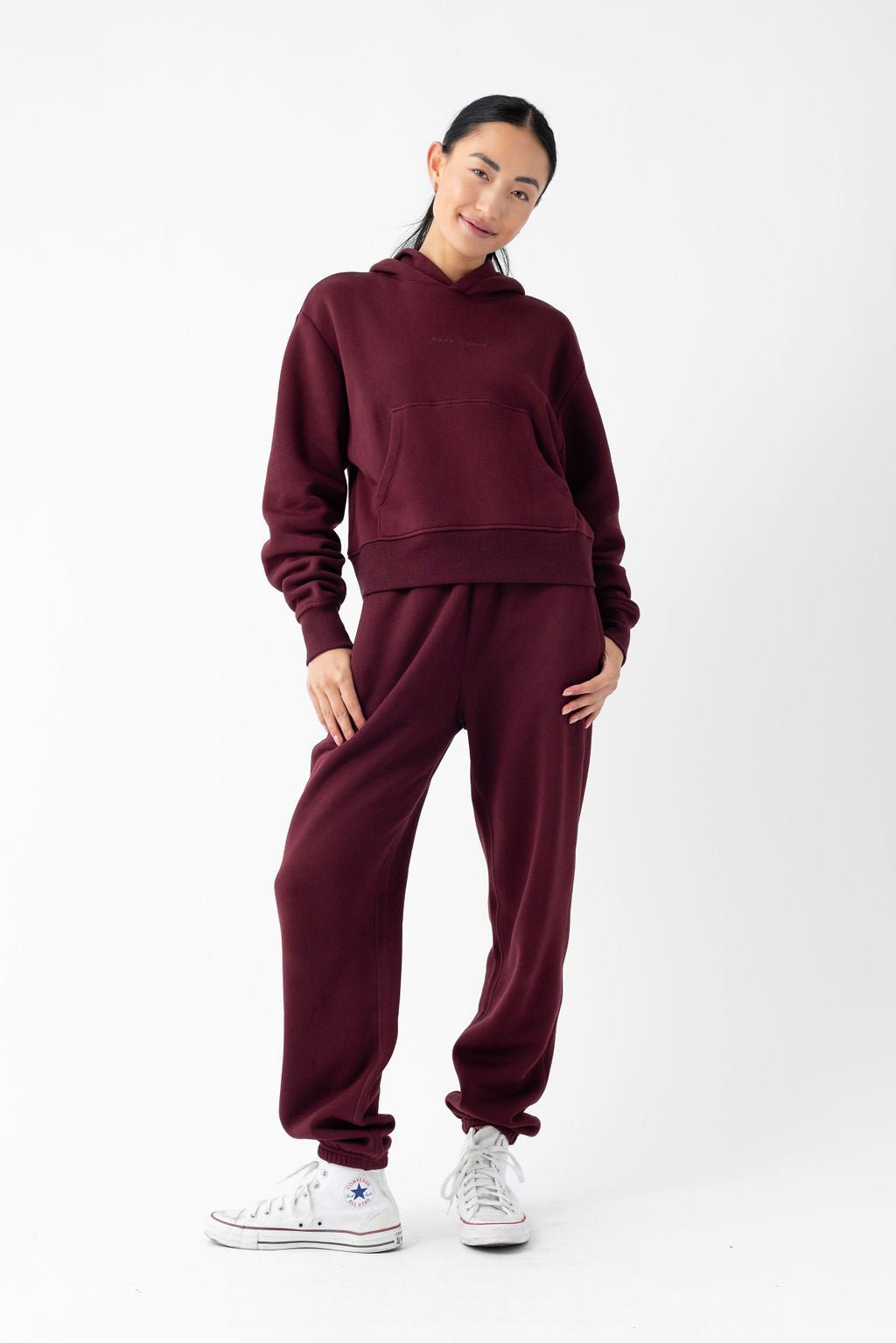 Person wearing maroon hoodie and sweatpants, posing against white background.