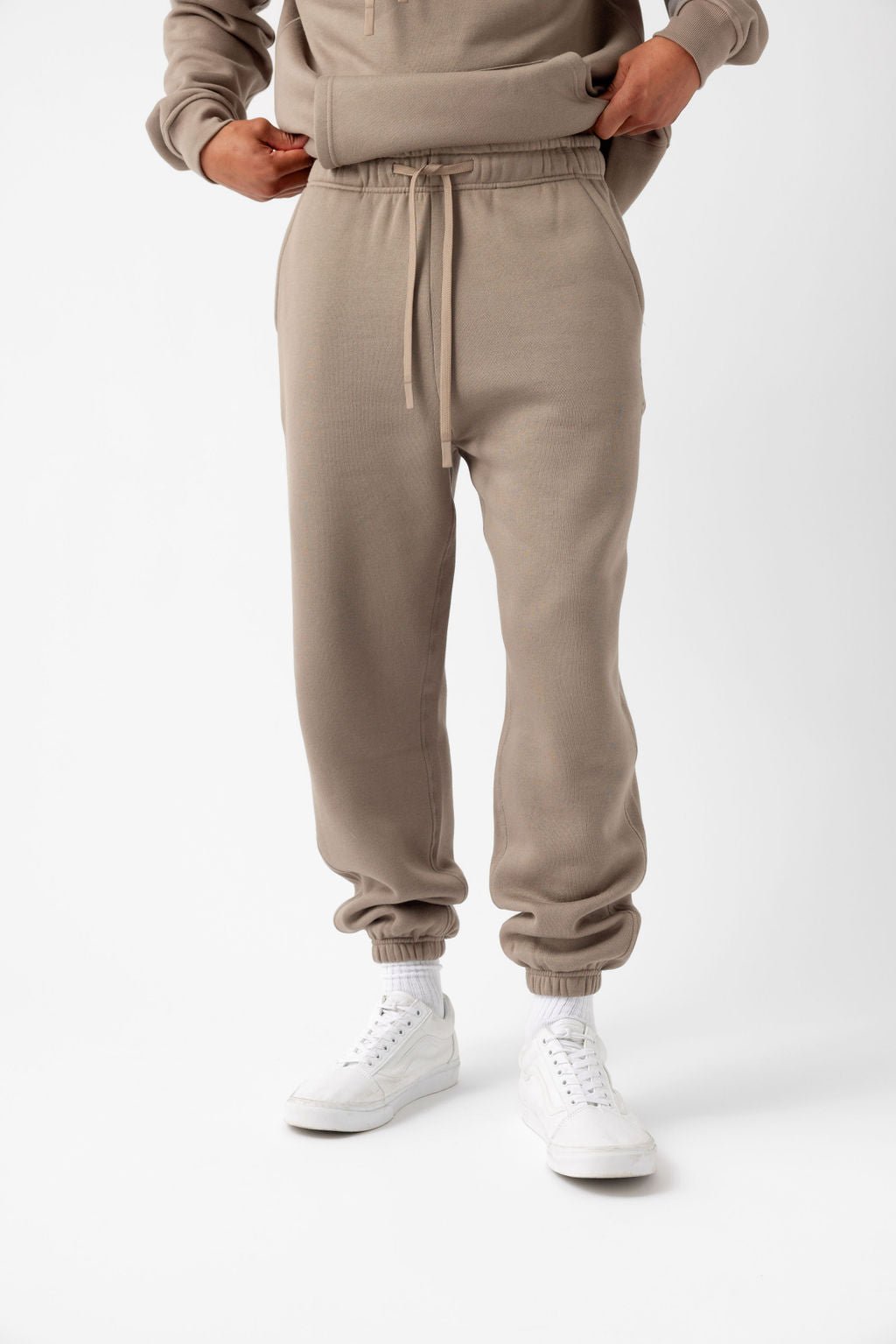 Person wearing beige joggers, white socks, and white sneakers on a white background.