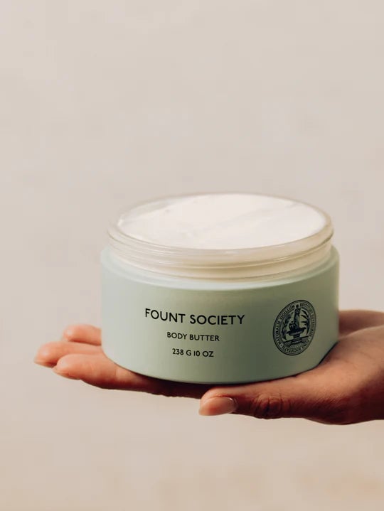 A hand holding a jar of Fount Society body butter.