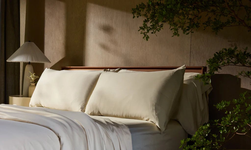 A neatly made bed with white pillows and bedside lamp.