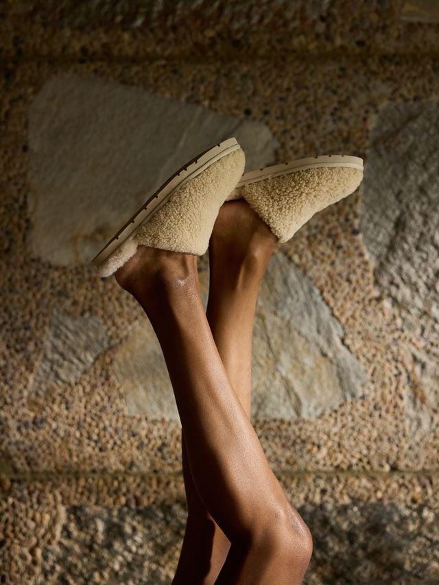 Feet in fuzzy slippers against a textured wall background.