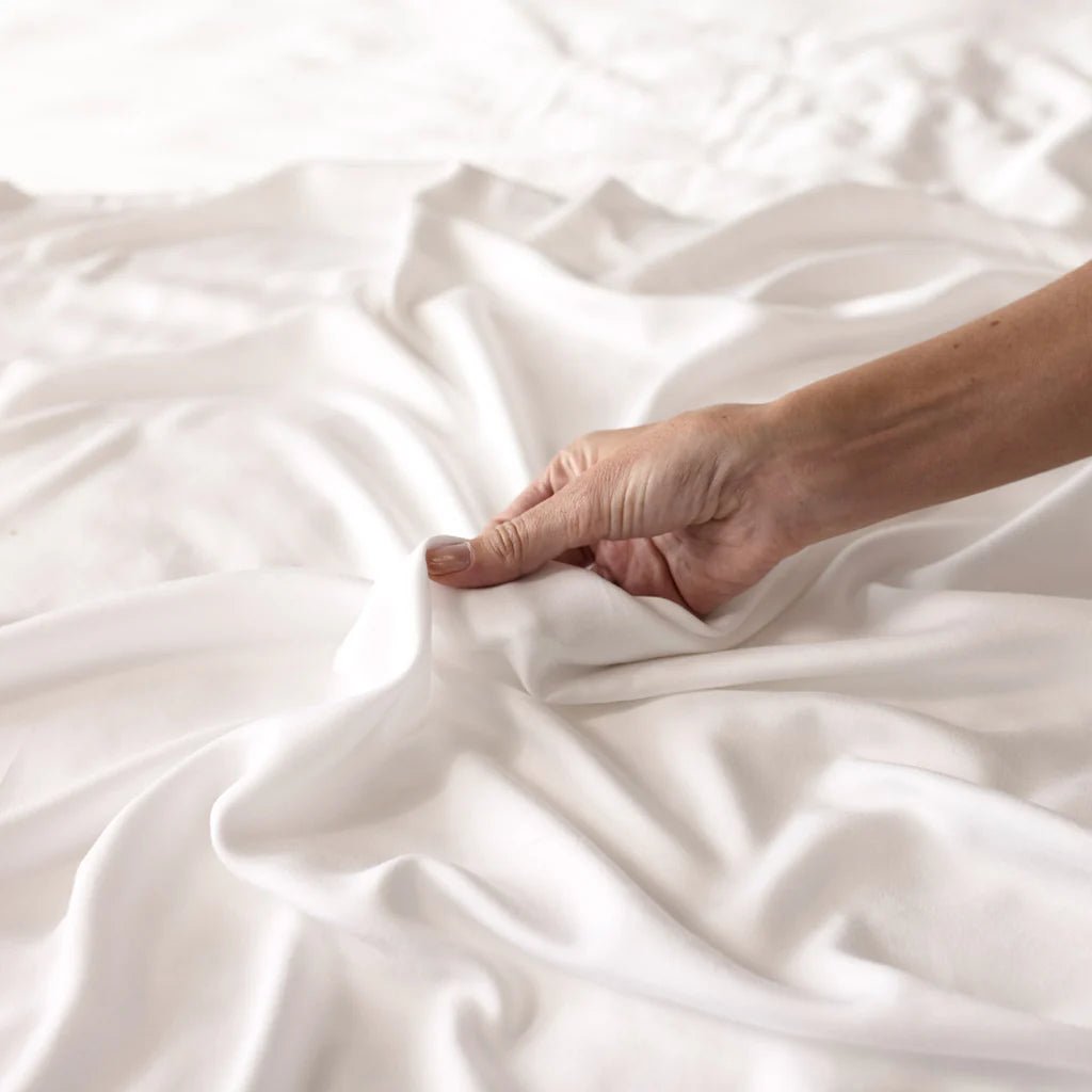 A hand gently holds soft, white fabric.