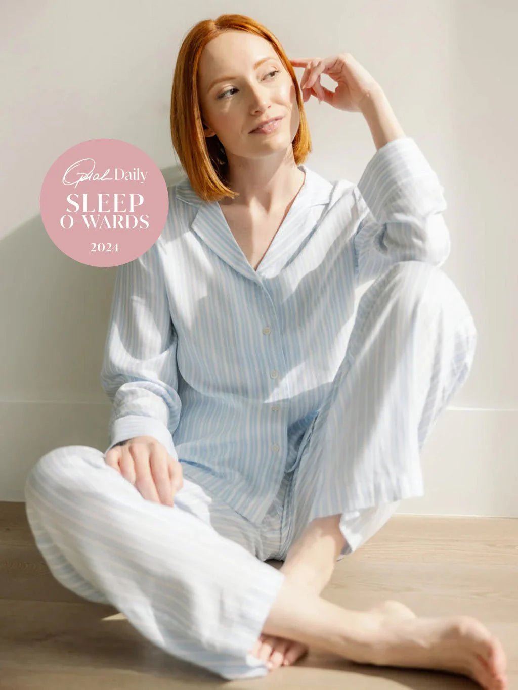 Person in light striped pajamas sitting on the floor, with 'Oprah Daily Sleep Awards 2021' text beside them.