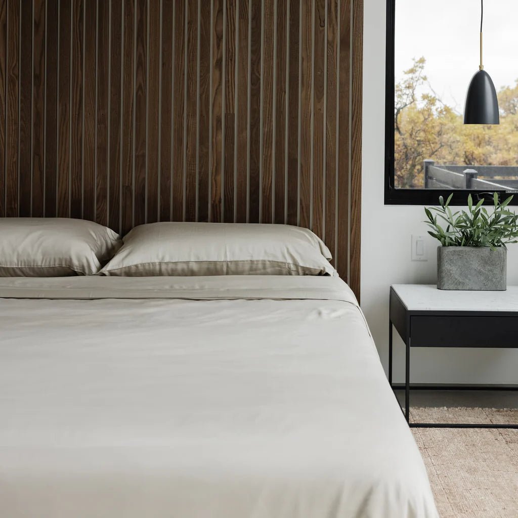 Modern bedroom with beige bedding, wooden accent wall, and a potted plant on a nightstand.
