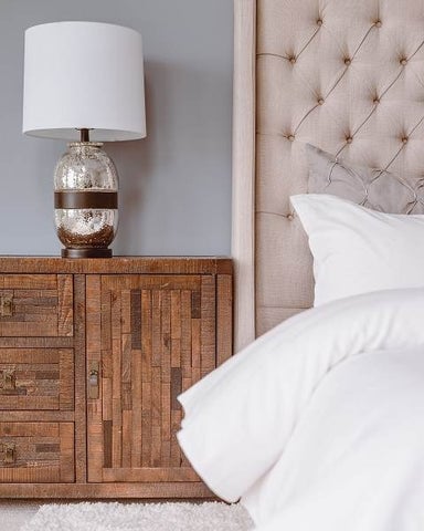 Wooden nightstand with lamp on top and upholstered headboard to the right