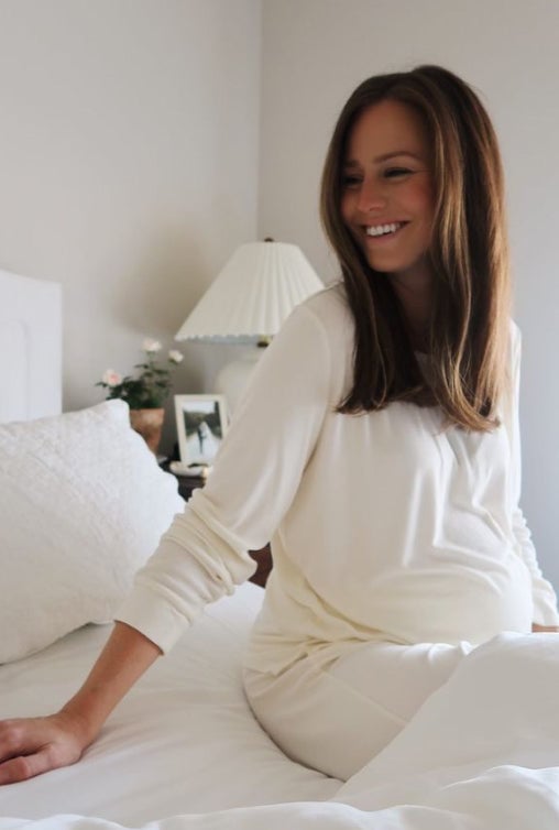 Woman wearing white loungewear sitting on bed.