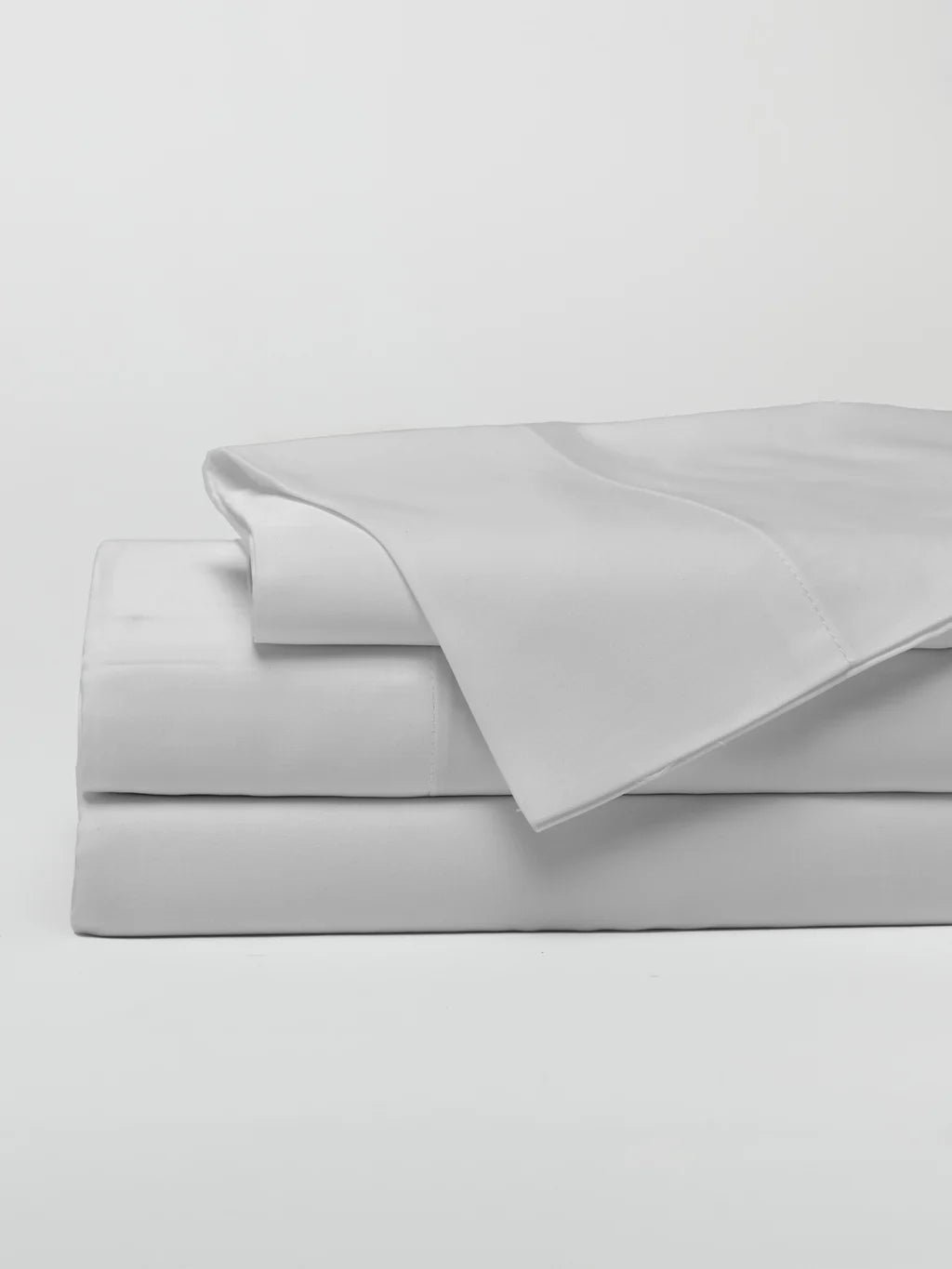 A stack of folded crisp white bed sheets on a white background.