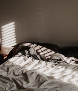 Dark room with sunlight streaming in through window onto wrinkled sheets