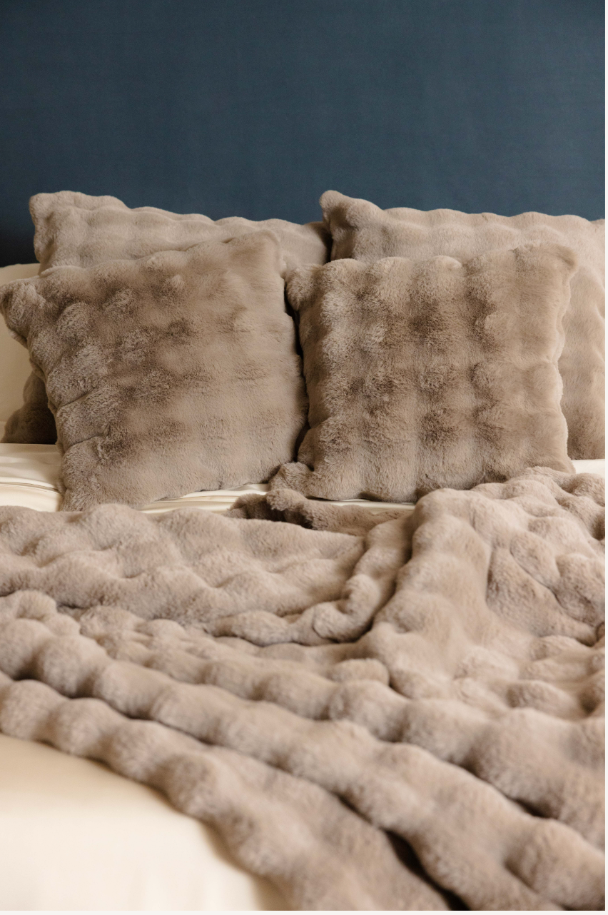 Soft textured beige pillows and blanket on a bed.