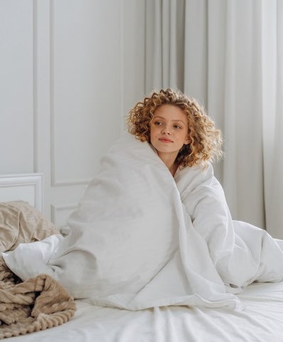 Young woman wrapped in a comforter on a bed